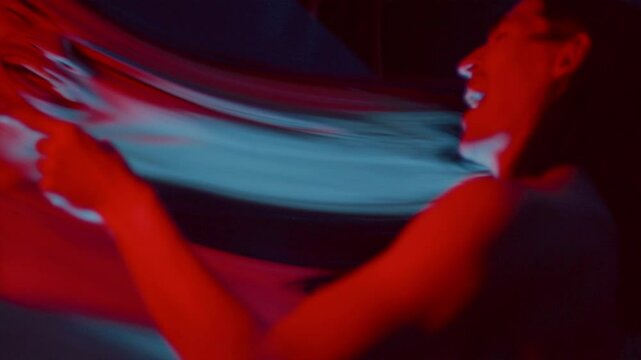 Mad man laughing evilly at his warped reflection in distorting mirror, clenching fists and expressing anger in dark studio with blue and red illumination