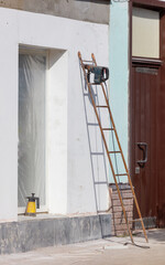 A ladder leaning against a building with a drill on top of it