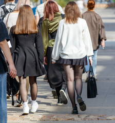 A group of people walking down a street, one of them wearing a white sweater