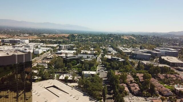 Aerial backwards shot of AIG Capital Service Building and parking cars in Woodland Hills, LA. Sunny day with main street and colorful trees in autumn.