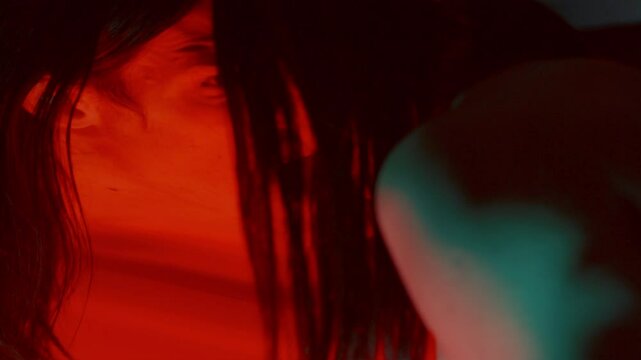 Creepy man pressing his face against distorting mirror, screaming madly with frightening expression in dark studio with red lighting