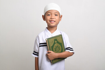 Portrait of smiling Muslim boy holding Quran isolated on white background