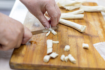 senior woman hand cut horseradish on wooden cutting board with knife