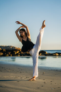 Woman performing a high leg stretch on the beach with graceful poise