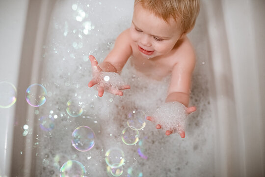 Toddler in bubble bath happily playing with bubbles