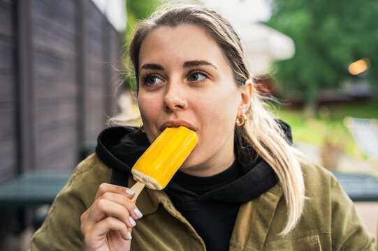 A young  woman eating a yellow ice-cream on a stick