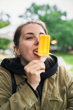 A young woman holding a yellow ice-cream on a stick