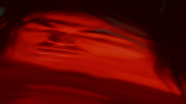 Astonished man staring in disbelief at his warped surreal reflection in distorting mirror in dark studio with red light