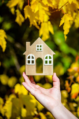 The symbol of the house in the girl's hand on the background of yellow leaves
