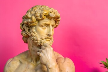 Aged marble statue against a vivid pink background with copy space, showing thoughtful expression in classical art form. Adds a playful twist with vibrant color. 