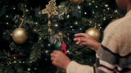 Over shoulder shot of unrecognizable kid decorating artificial evergreen tree with Christmas ornaments