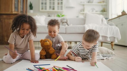 Diverse adopted children playing together in living room, Black and Caucasian. Happy childhood, charming little kids drawing by colored pencils on floor in cozy living room, happiness and joy, family