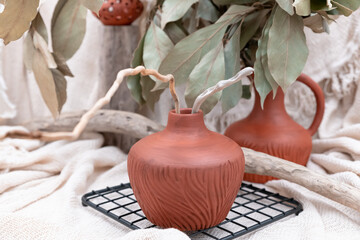 Still life of vase, jug and candlestick and red terracotta with driftwood branches, beige mesh tablecloth and bay leaves