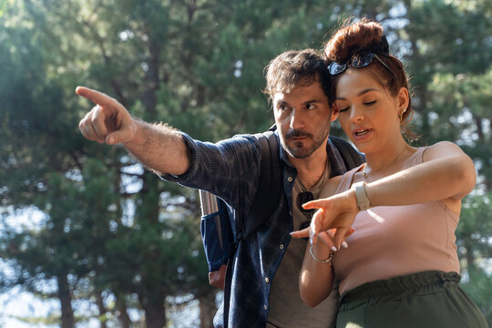 Couple hiking in forest checking smartwatch navigation map, diverse young hikers using digital device outdoors