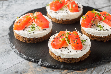 Mini cheesecake salmon with cream cheese, sesame and micro greens close-up on slate plate on the table. Horizontal
