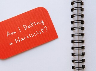 Orange card on notebook written Am I Dating a Narcissist? - question to ask if one have troubled or...