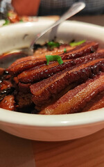 A bowl of meat with a spoon in it. Pork belly prepared in traditional Chinese style