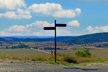 A blank signpost is standing in a field with a cloudy sky in the background