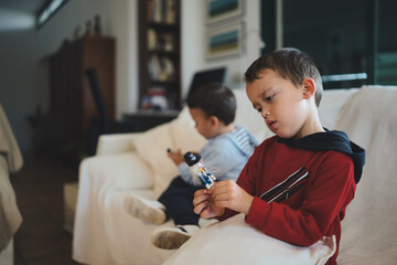 Two young brothers, one playing with a small toy and the other using a smartphone, spend time together in their living room