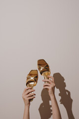 Stylish Gold Sandals Raised Against Light Backdrop. Modern Fashion Trends and Unique Footwear Design. Shadows and Minimalist Aesthetic