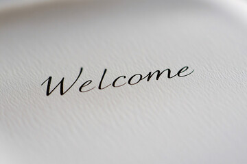 Fototapeta premium closeup of elegant black cursive welcome text on white textured paper evoking warmth and hospitality in a minimalist style 