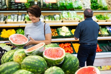 Elderly woman chooses watermelon in fruit and vegetable section