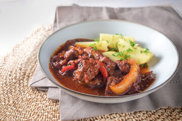 Goulash with bell pepper in Hungarian style served with potatoes and parsley garnish on a light gray plate, spicy meat dish for dinner or lunch, copy space, selected focus