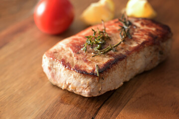 Roasted pork loin steak with herbs on a wooden board, homemade hearty meat dish, copy space, selected focus