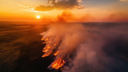 Fototapeta premium Aerial perspective of wildfire consuming grassland at sunset creating a smoke plume Representation of environmental disaster and climate change issues