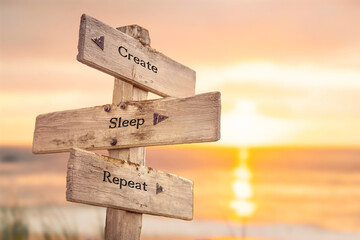 create sleep repeat text quote written on wooden signpost by the sea during sunset and golden hour.