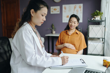 Medical professional consulting pregnant woman in office setting, focusing on healthcare treatment and patient care while observing pregnancy health and wellness