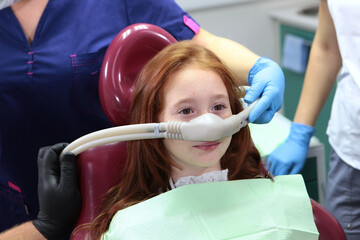 Little girl is injected with an inhalation sedation during dental treatment at dental clinic. Dental treatment for child. Anesthesia for children in dental treatment.