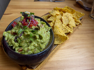 Detail shot of delicious nachos with guacamole and natural tomato, on a wooden board.