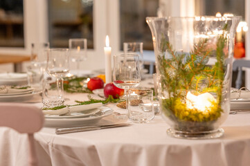 Festively decorated dinner table set for a Christmas celebration, with lit candles, fresh greenery, and seasonal decorations, exuding a warm and inviting holiday ambiance