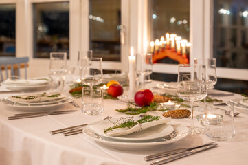 Festively decorated dinner table set for a Christmas celebration, with lit candles, fresh greenery, and seasonal decorations, exuding a warm and inviting holiday ambiance