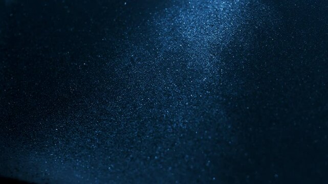 Little grains of sand falling in abstract slow motion under blue light. 
