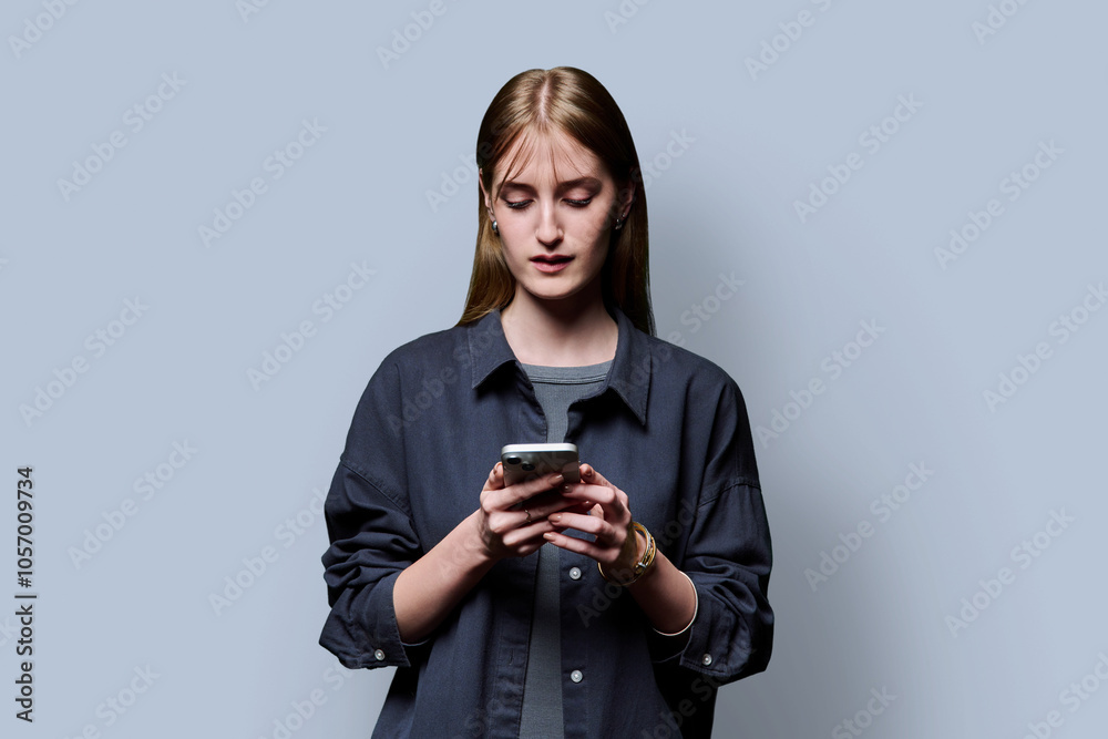 Wall mural young beautiful woman using smartphone on grey studio background