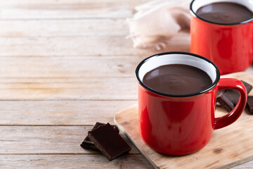 Hot chocolate drink in red mug on wooden table. Copy space