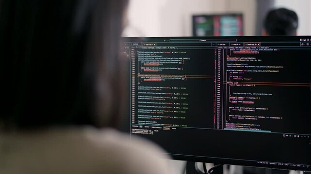 Concentrated Asian female developer debugging software on a multi-monitor setup, engaged in complex problem-solving.