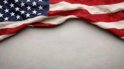 Obraz premium A worn American flag drapes over a neutral surface, showcasing its iconic colors of red, white, and blue.