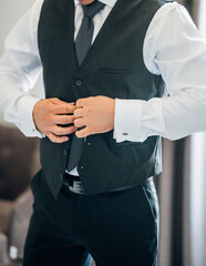 A man puts on a business suit vest over a white shirt with a tie. Men's business fashion.