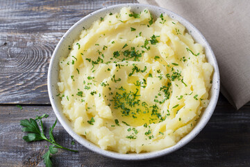 Mashed potatoes with melted butter and herbs in a gray ceramic bowl on a wooden table