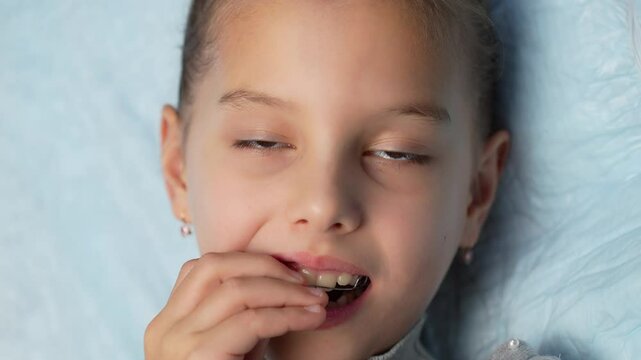 Little girl putting teeth braces for teeth correction in her mouth, close-up. Child putting teeth retainers