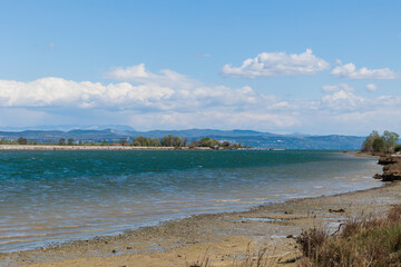 costa lungo un largo canale acquatico che fluisce nel Golfo di Trieste, nel Mare Adriatico settentrionale, con vista su colline e montagne lontane, di giorno
