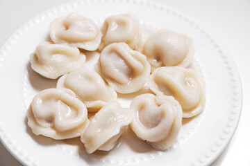 Boiled dumplings are arranged in a circle on a white plate. The plate with dumplings is set against a light background, creating a simple and appetizing composition.
