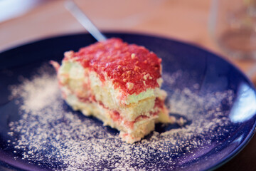 dettagli macro di un dessert dolce a base di pan di spagna e crema di colore rosso, su un piatto blu