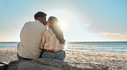 Kiss, beach and back of couple relax on getaway, vacation or holiday for romance together. Love, travel and man and woman sitting on sand by tropical ocean on seaside date on summer weekend trip.