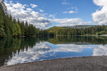 ampia vista panoramica da una delle sponde del lago di Fusine inferiore, nel nord est Italia, col cielo e la foresta che si specchiano sull'acqua, di pomeriggio, in estate