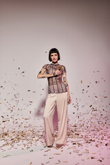 A fashionable woman poses confidently while surrounded by colorful confetti.