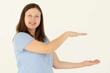 Young confident woman showing logo on empty space between arms. Smiling girl inviting or advertising promo deal, pointing hands right and looking at camera, white background.